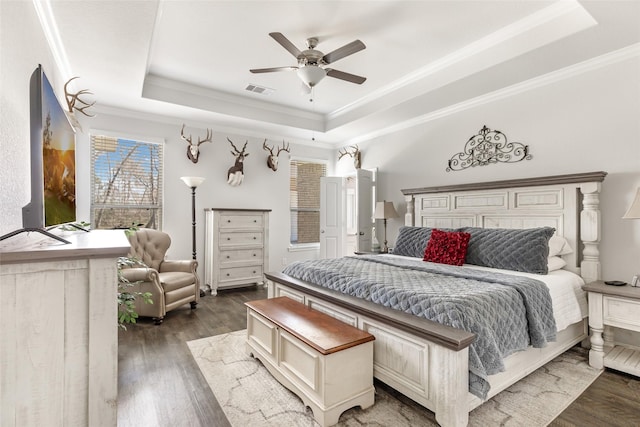 bedroom with visible vents, a tray ceiling, ornamental molding, wood finished floors, and a ceiling fan