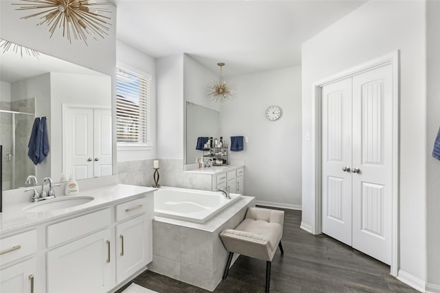 bathroom featuring vanity, wood finished floors, baseboards, a bath, and a shower with door