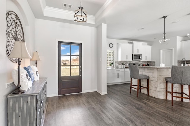 entrance foyer featuring visible vents, dark wood-type flooring, a tray ceiling, crown molding, and baseboards