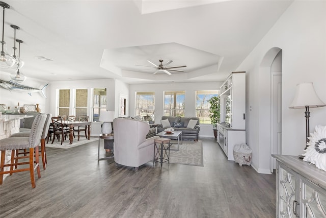 living area featuring visible vents, a raised ceiling, dark wood-type flooring, a ceiling fan, and baseboards