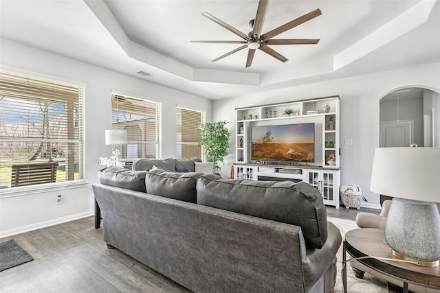 living area featuring a tray ceiling, plenty of natural light, visible vents, and ceiling fan