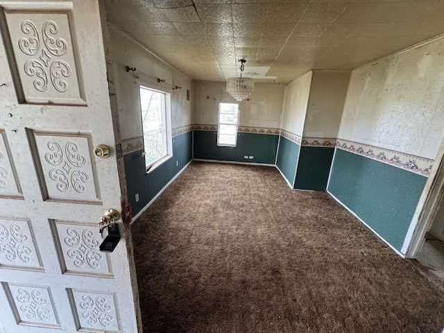 empty room with a chandelier, wainscoting, baseboards, and carpet floors