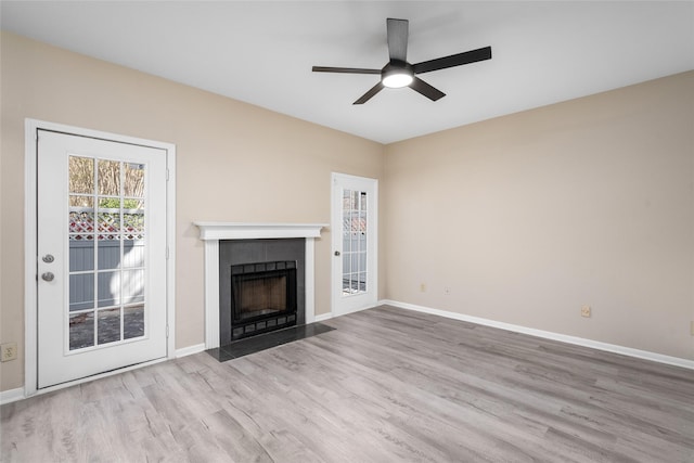 unfurnished living room featuring baseboards, a fireplace with flush hearth, wood finished floors, and a ceiling fan