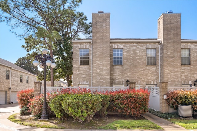 exterior space with cooling unit, fence, brick siding, and a chimney