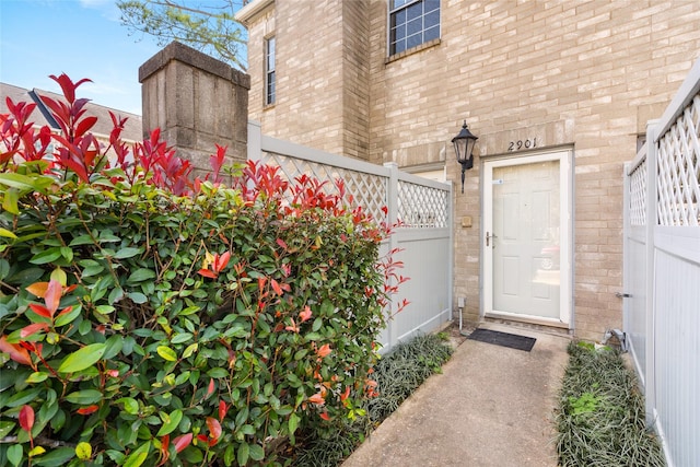 view of exterior entry featuring brick siding and fence