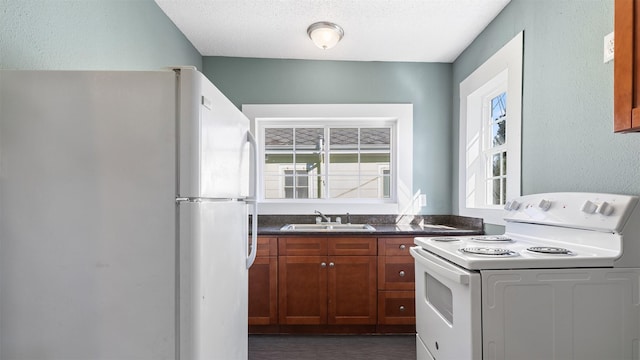 kitchen featuring a sink, dark countertops, a textured ceiling, white appliances, and brown cabinetry