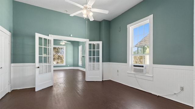 empty room featuring cooling unit, ceiling fan, french doors, wood-type flooring, and wainscoting