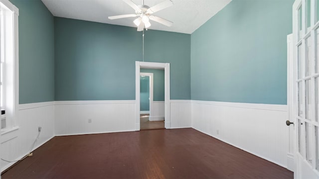 empty room featuring wood finished floors, wainscoting, and ceiling fan