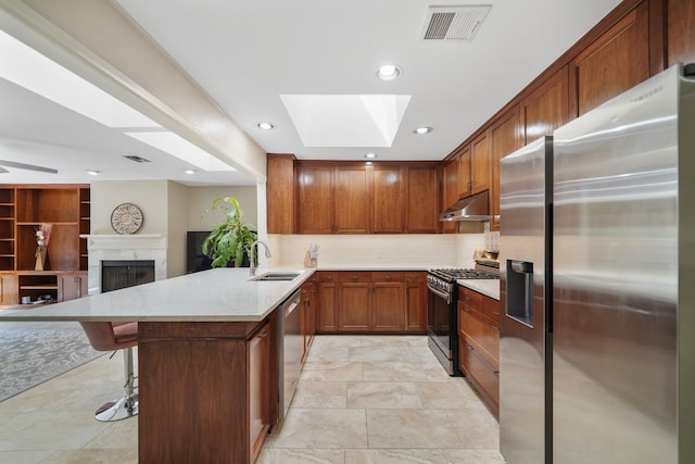 kitchen with visible vents, under cabinet range hood, appliances with stainless steel finishes, a fireplace, and a sink