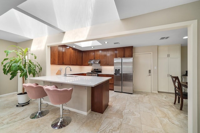 kitchen featuring a peninsula, a skylight, a sink, under cabinet range hood, and appliances with stainless steel finishes