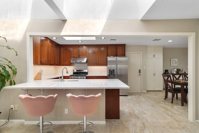 kitchen featuring under cabinet range hood, a sink, tasteful backsplash, appliances with stainless steel finishes, and a peninsula