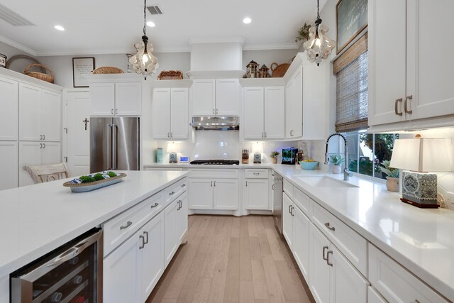 kitchen with beverage cooler, ornamental molding, a sink, under cabinet range hood, and stainless steel appliances