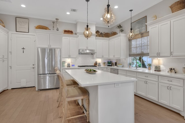 kitchen with visible vents, freestanding refrigerator, white cabinets, under cabinet range hood, and a center island