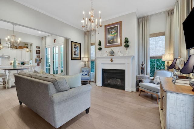 living room with a glass covered fireplace, a notable chandelier, light wood-style floors, and ornamental molding