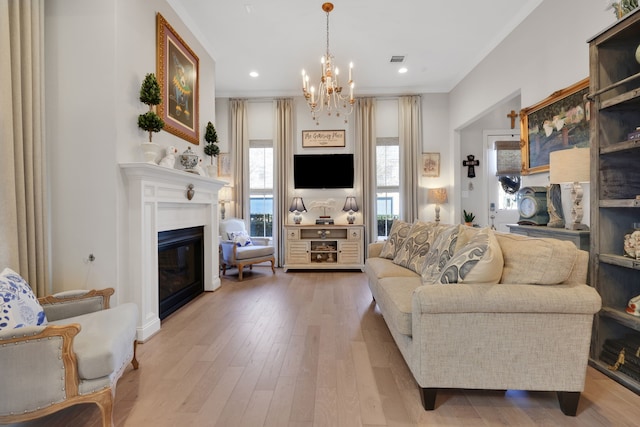 living room with visible vents, wood finished floors, a glass covered fireplace, crown molding, and a chandelier