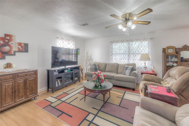 living area featuring light wood finished floors, visible vents, a textured ceiling, and ceiling fan