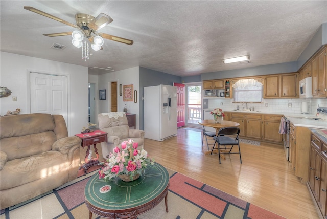 living room with light wood-type flooring, visible vents, a textured ceiling, and a ceiling fan