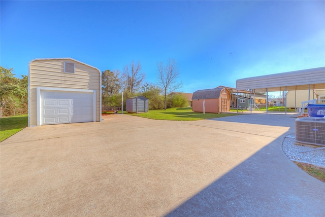 view of yard featuring a detached garage, concrete driveway, central AC, an outbuilding, and a storage unit