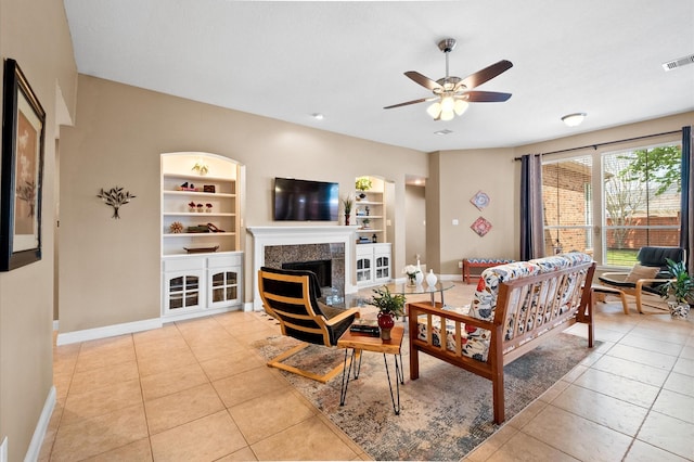 living area with built in shelves, light tile patterned flooring, a fireplace, baseboards, and ceiling fan