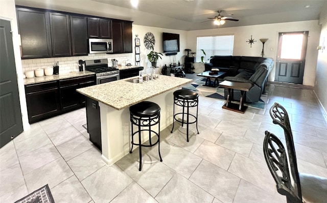 kitchen featuring a ceiling fan, a sink, decorative backsplash, stainless steel appliances, and open floor plan