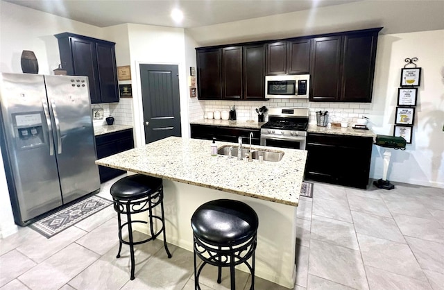 kitchen with backsplash, light stone countertops, a breakfast bar, stainless steel appliances, and a sink