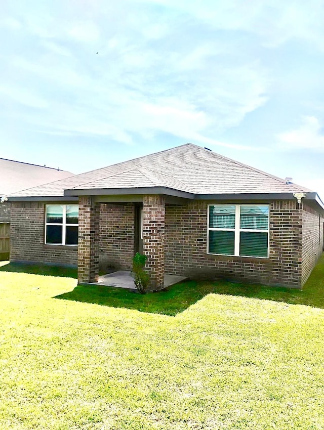 rear view of property with a patio, brick siding, roof with shingles, and a lawn