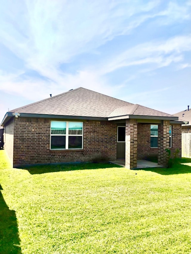 rear view of property with brick siding, a lawn, a patio, and roof with shingles