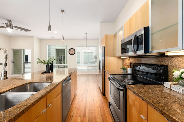 kitchen featuring pendant lighting, a sink, backsplash, stainless steel appliances, and light wood finished floors