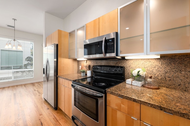 kitchen featuring light wood-style flooring, glass insert cabinets, dark stone counters, appliances with stainless steel finishes, and decorative backsplash