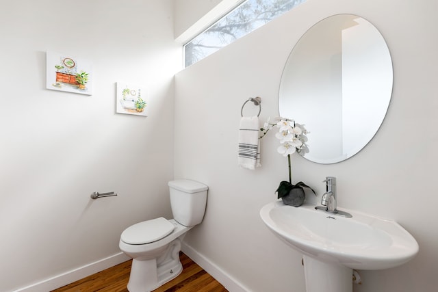 half bathroom featuring wood finished floors, toilet, baseboards, and a sink