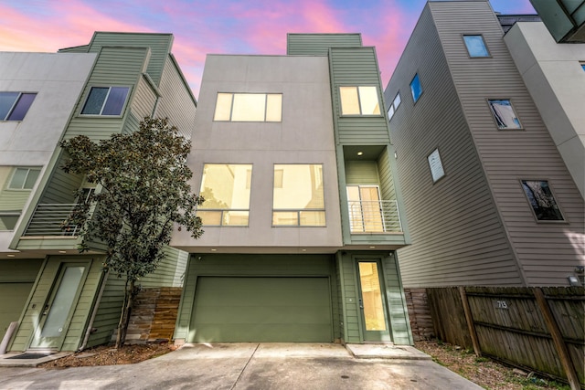 back of property with a balcony, fence, concrete driveway, a garage, and stone siding