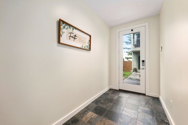 doorway to outside with baseboards and stone tile flooring