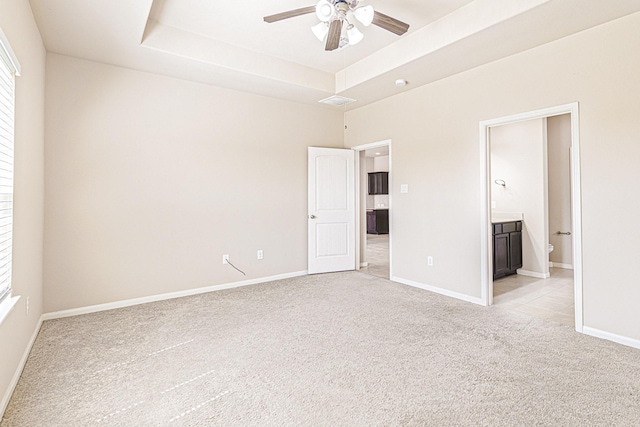 unfurnished bedroom featuring multiple windows, a raised ceiling, light carpet, connected bathroom, and baseboards