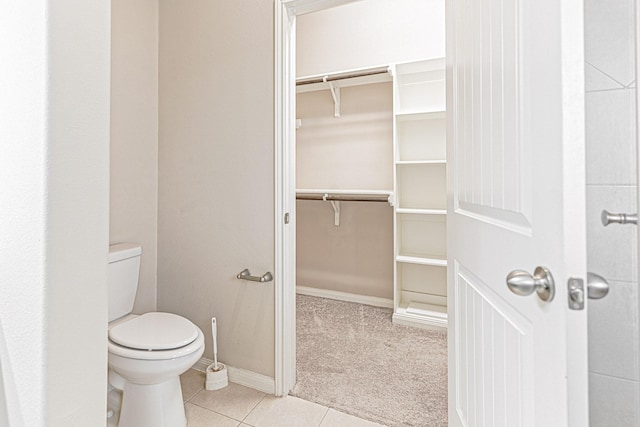 bathroom with tile patterned floors, a spacious closet, toilet, and baseboards