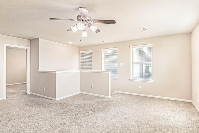 carpeted spare room with visible vents, baseboards, and ceiling fan