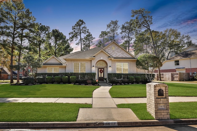 view of front of house with brick siding, a lawn, roof with shingles, and fence