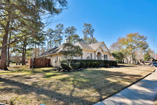 view of side of home with stucco siding, a chimney, a yard, and fence