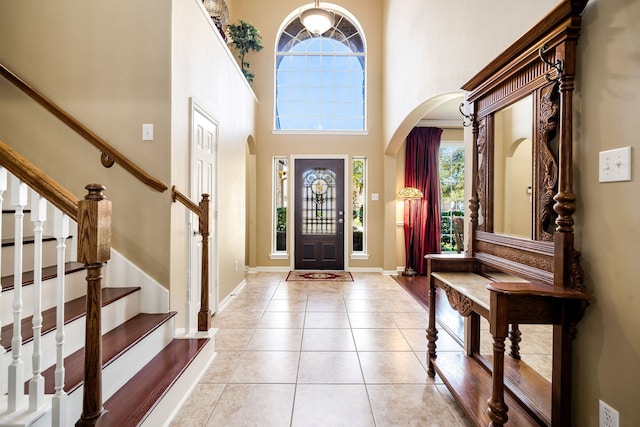 foyer entrance featuring tile patterned floors, stairway, arched walkways, baseboards, and a towering ceiling