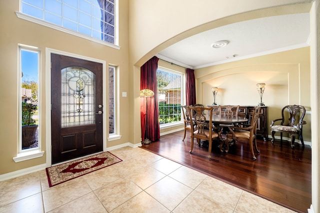 tiled entryway featuring crown molding, baseboards, and arched walkways