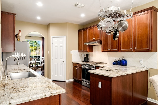 kitchen featuring a peninsula, arched walkways, a sink, under cabinet range hood, and stainless steel gas stove