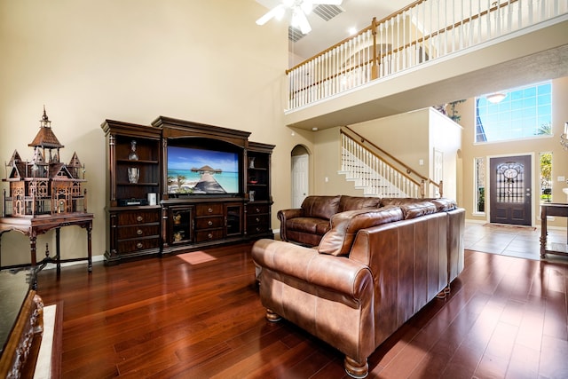 living room with hardwood / wood-style flooring, a ceiling fan, arched walkways, and a towering ceiling