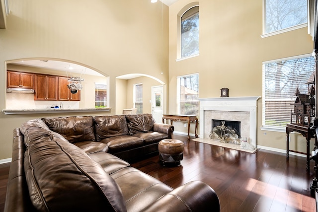 living area with baseboards, a fireplace, a high ceiling, arched walkways, and dark wood-style flooring