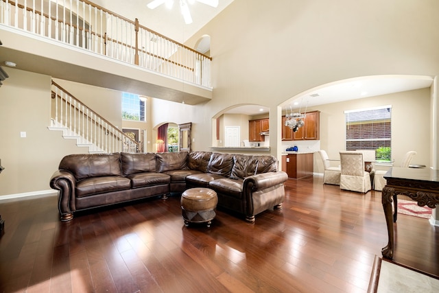 living area featuring arched walkways, plenty of natural light, dark wood-style floors, and a ceiling fan