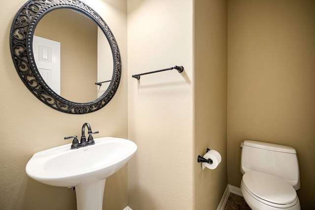 half bathroom featuring toilet, baseboards, and a sink