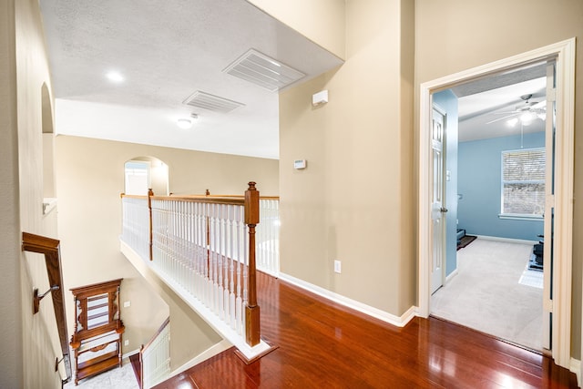 corridor featuring wood finished floors, an upstairs landing, arched walkways, and baseboards