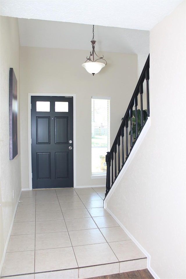 foyer entrance with stairway, light tile patterned floors, and baseboards