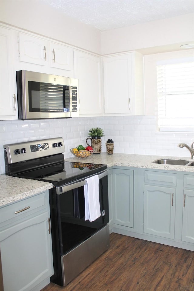 kitchen featuring dark wood-type flooring, a sink, tasteful backsplash, appliances with stainless steel finishes, and white cabinets