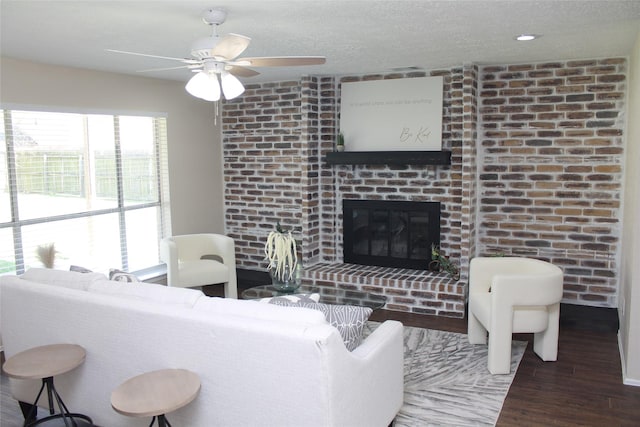 living area with a textured ceiling, a brick fireplace, wood finished floors, and ceiling fan