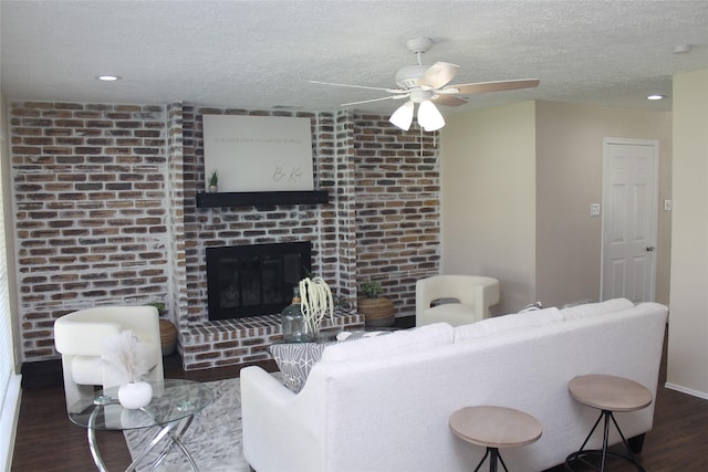 living area with a textured ceiling, wood finished floors, recessed lighting, a brick fireplace, and ceiling fan