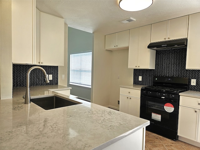 kitchen featuring visible vents, under cabinet range hood, a sink, tasteful backsplash, and black gas stove